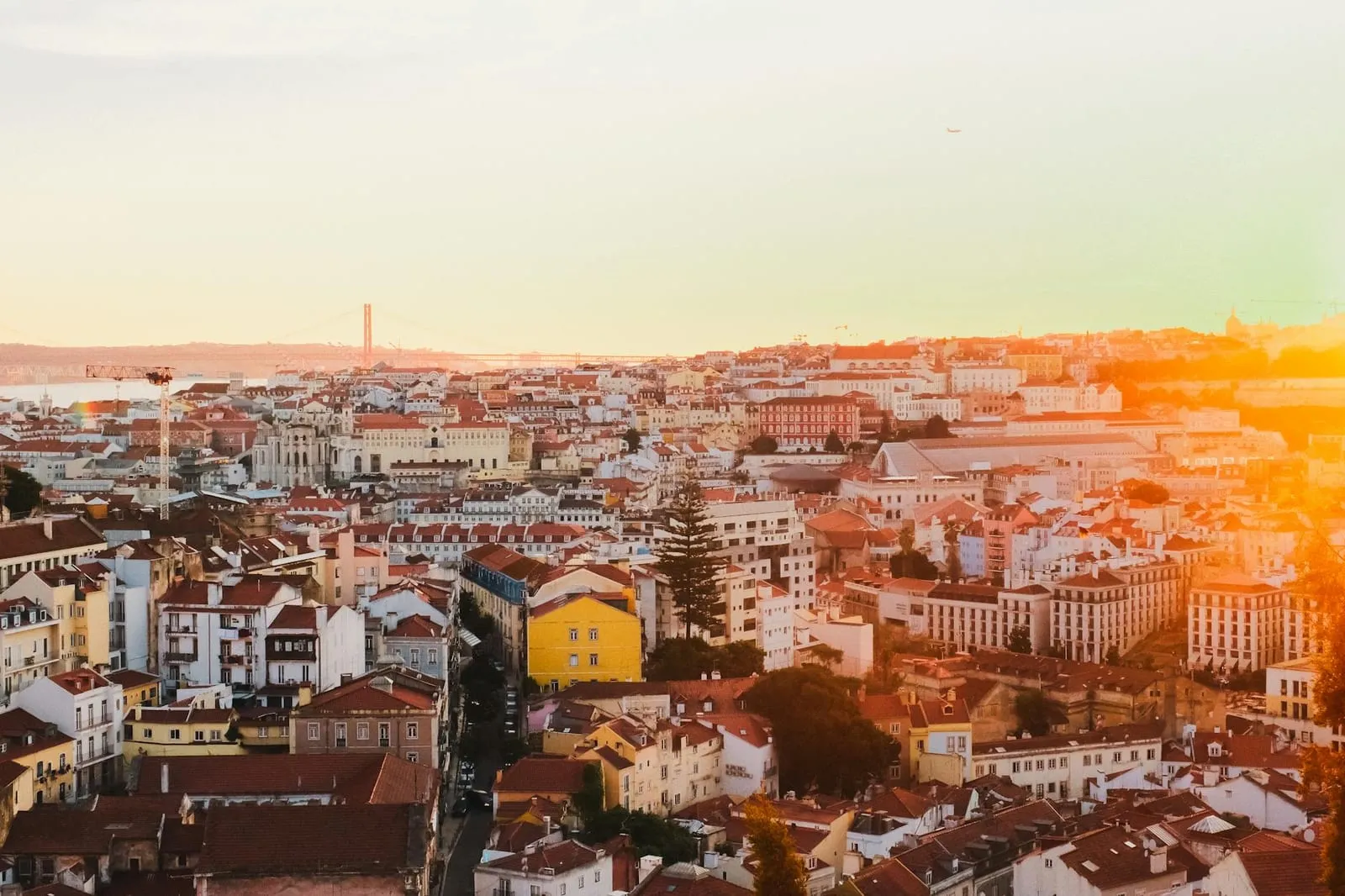 Vista de Lisboa ao pôr do sol, com telhados e rio Tejo em fundo