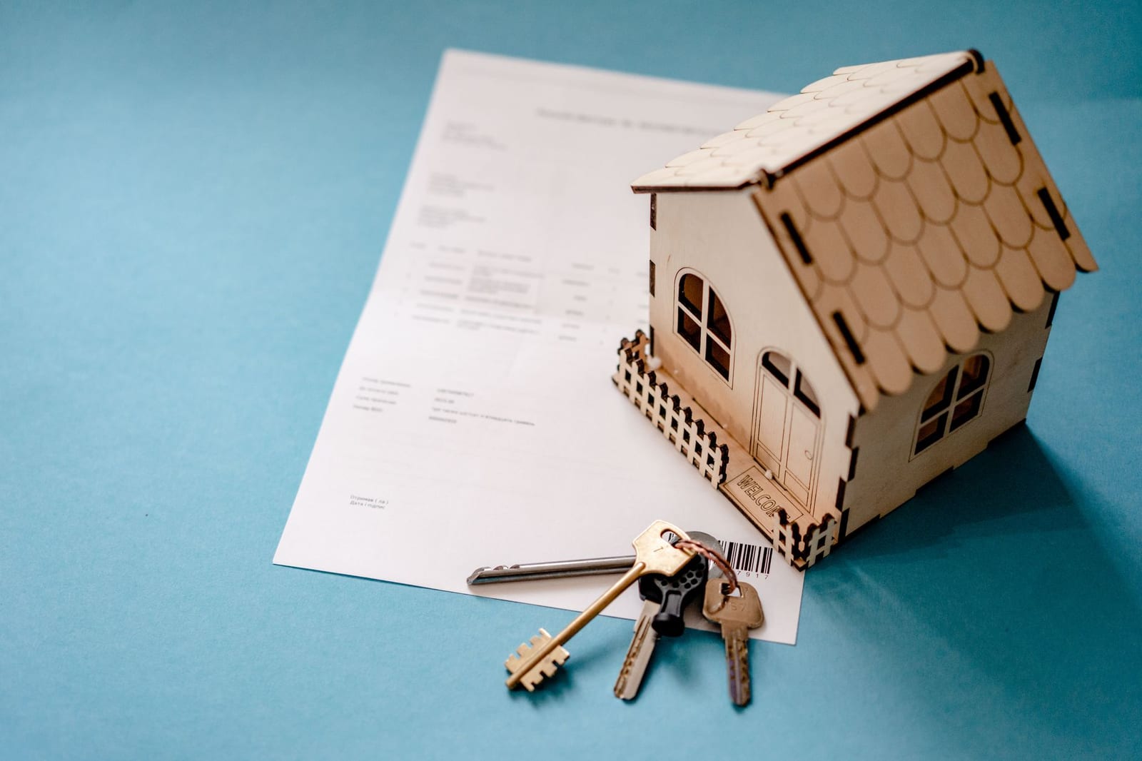 Casa em miniatura de madeira sobre um contrato, com molho de chaves ao lado.